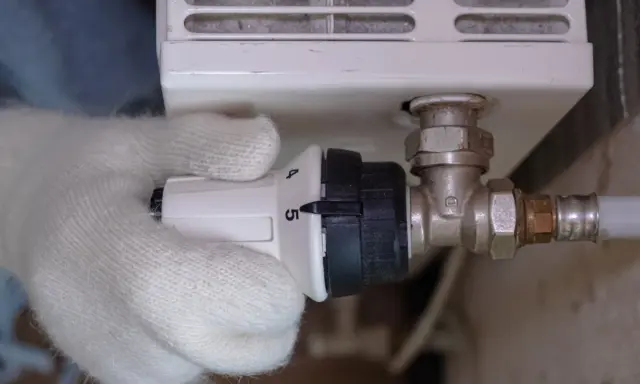 Main tenant ajuste le thermostat, réglant la température de son radiateur. Le raccord diélectrique montage est visible.