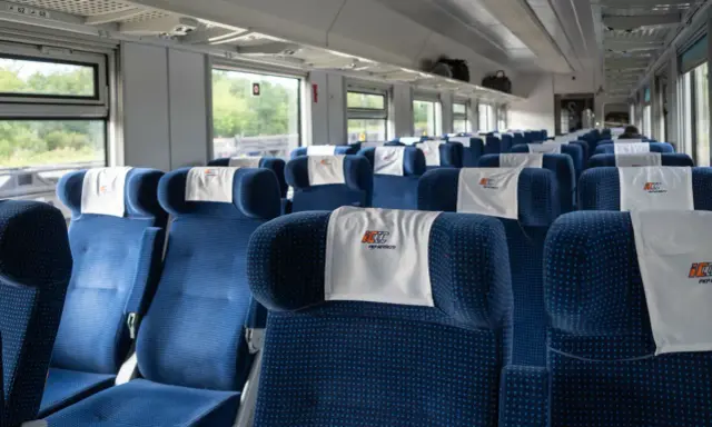 Puste niebieskie siedzenia w wagonie PKP Intercity z zagłówkami z logo.