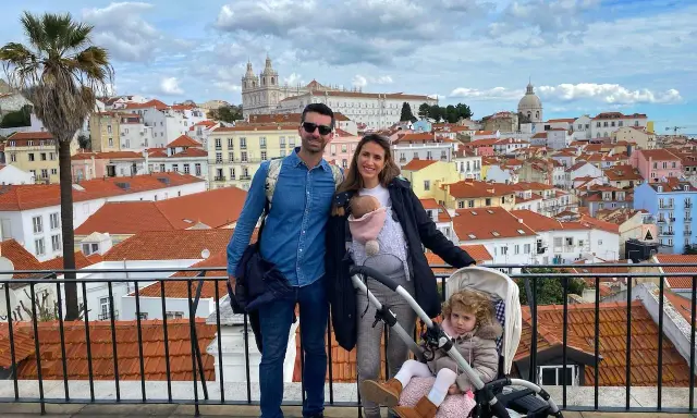 Familia disfrutando de las vistas de Lisboa con niños. Un bebé en portabebés y una niña en carrito, con la ciudad de tejados naranjas de fondo.