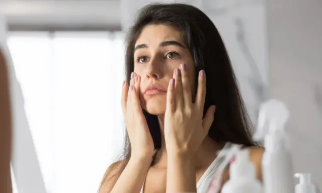 Donna preoccupata si tocca il viso, notando i segni dello stress sulla pelle.