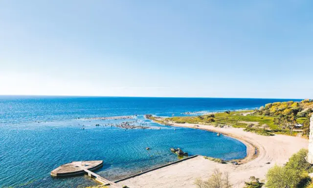 En vacker vy över ett vattenland på Gotland med en sandstrand, klart blått hav och gröna kullar.