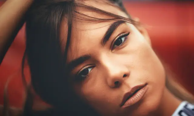 Portrait d'une jeune femme aux gros sourcils, la main dans les cheveux, regard intense.