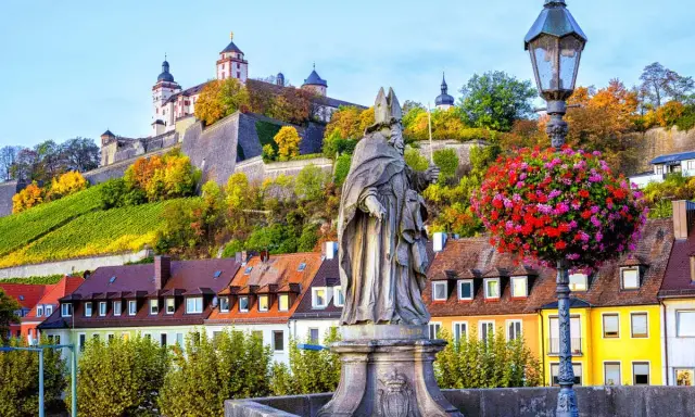 Statua sul ponte di Würzburg, con la fortezza in cima alla collina e i vigneti. Perfetto per un itinerario di 7 giorni sulla Romantische Straße.