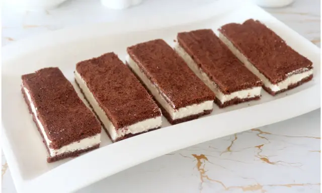 Sei fette di torta kinder fetta al latte, con pan di spagna al cacao e crema bianca, disposte su un piatto bianco.