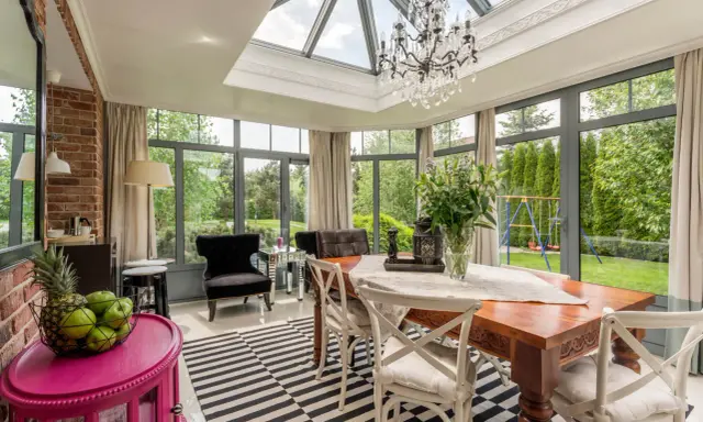 Une élégante verrière d'extension de maison baigne de lumière cette salle à manger, offrant une vue imprenable sur le jardin verdoyant.