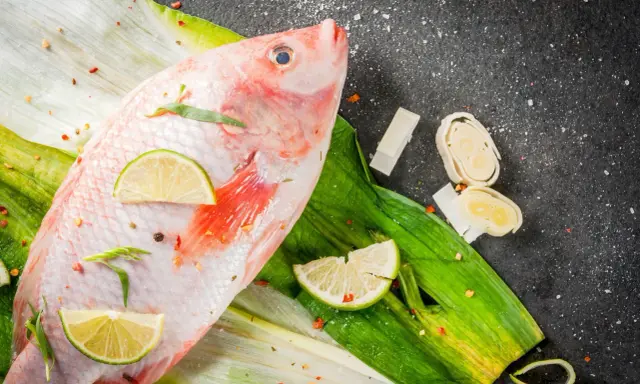 Cała ryba tilapia, przyprawiona chili i limonką, leży na zielonych liściach. Czy to tilapia, co to za ryba?