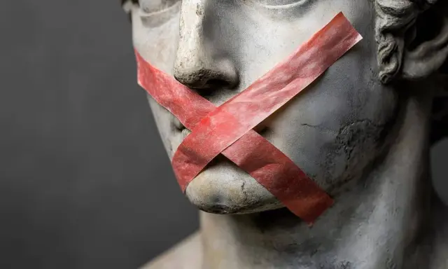 Busto di statua con nastro rosso a X sulla bocca, un esempio di antitesi tra arte e censura.