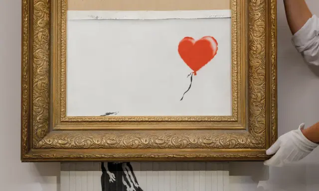 A framed Banksy artwork featuring a red balloon, hinting at how is Banksy rich.