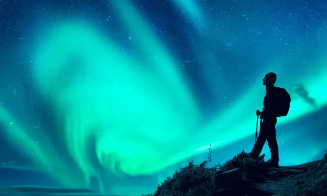 Vandrare ser norrsken över en stjärnklar himmel. En magisk upplevelse att fota norrsken i Lappland.