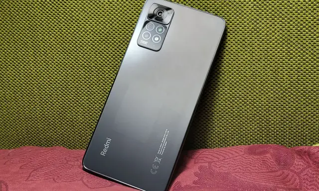 Elegancki, szary Redmi Note 11 Pro 5G Plus z aparatem 108MP na tle zielonej i bordowej tkaniny.