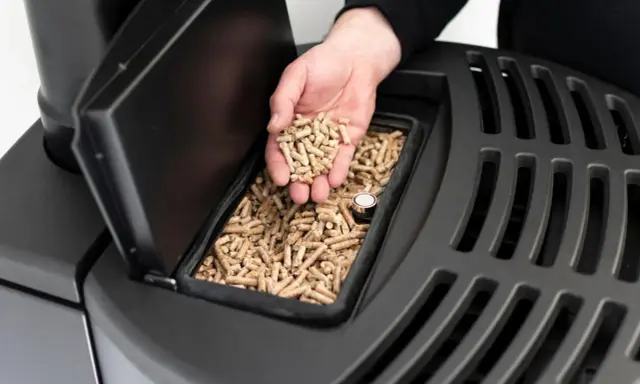 Mano sosteniendo **que es el pellet**, combustible para estufas, listo para ser añadido.