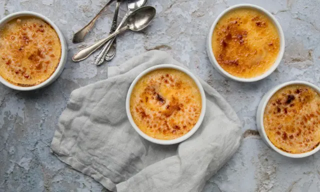 Quatre crèmes brûlées dorées, prêtes à être dégustées. La croûte caramélisée de cette crème catalane invite à la gourmandise.