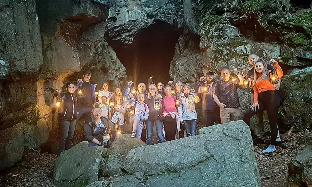 Grupa ludzi z latarniami przy skalnej grocie, odkrywająca tajemnice szlaku walońskiego.