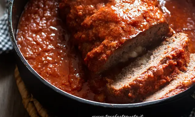 Un succulento polpettone ripieno al forno, affogato in un sugo rosso e invitante, con una fetta tagliata che rivela un cuore filante.