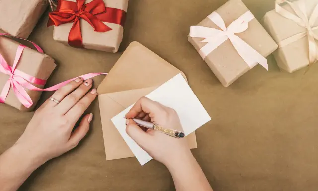 Piszę kartkę z podziękowaniem za zaproszenie na imprezę. Wokół leżą prezenty owinięte w papier i ozdobione wstążkami.