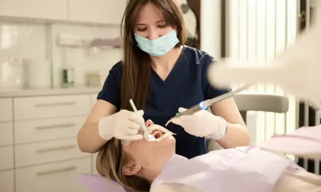 Dentystka w masce i rękawiczkach wykonuje zabieg u pacjentki w gabinecie stomatologicznym.