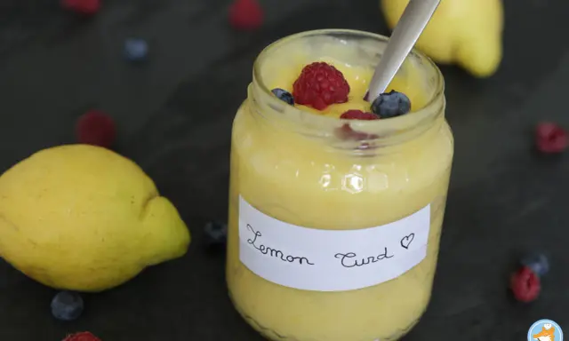 Un pot de lemon curd maison, garni de framboises et myrtilles, avec des citrons frais et des baies éparpillés.