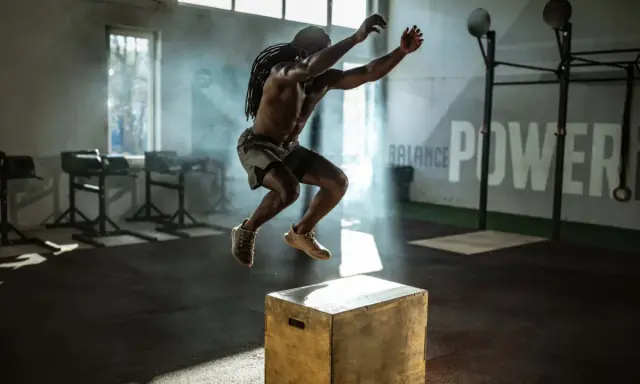 Mann mit Dreadlocks macht explosive Box Jumps in einem nebeligen Fitnessstudio.