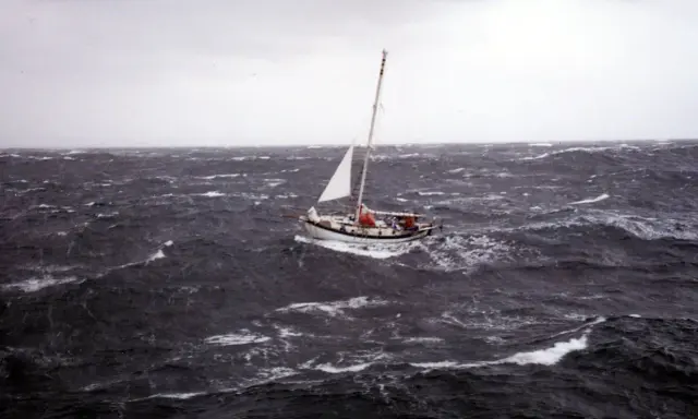 Un voilier affronte une mer agitée, sa voile blanche tendue. La mise à la cape est une manœuvre de survie face aux éléments déchaînés.