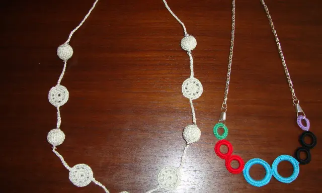 Dos collares de ganchillo y abalorios: uno blanco con esferas y círculos calados, y otro con cadena plateada y aros de colores.