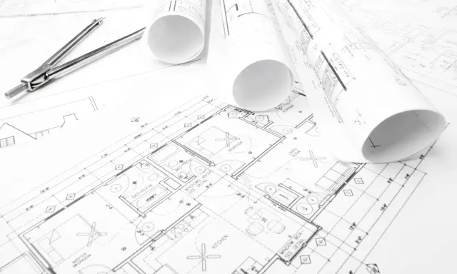 Projekt budowlany domu z widocznym cyrklem i zwiniętymi planami.