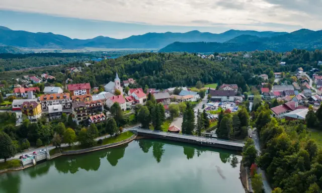Malownicze miasteczko w Chorwacji, otoczone zielonymi wzgórzami i górami. Jezioro odbija kolorowe dachy domów.