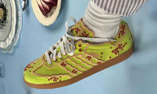 Jaskrawozielone buty Adidas z haftowanymi kwiatami wiśni i różowymi lamówkami, prawdopodobnie najdroższe buty Adidas, prezentowane na błękitnym tle.