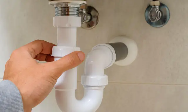 Mano ajustando la altura del desague del lavabo, tubería blanca de PVC bajo el lavamanos.