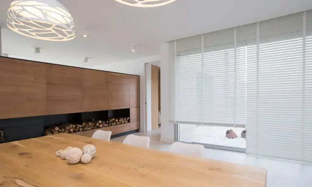 Un salon moderne avec un grand mur en bois, une table en bois et un type de store vénitien blanc qui habille une large fenêtre.
