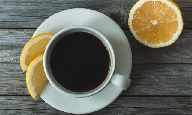 Eine Tasse schwarzer Kaffee mit Zitrone und Zitronenscheiben auf einem Holztisch.