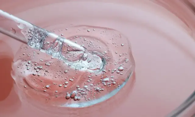 Goutte d'un sérum transparent avec des bulles, sur fond rose. C'est une illustration de ce que sont les peptides, des éléments clés pour la peau.