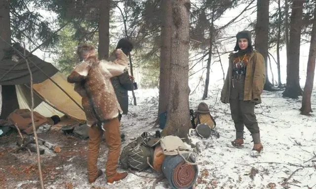Zimowy obóz bushcraftowy. Dwie osoby w strojach z epoki, namiot, plecaki i sprzęt survivalowy.