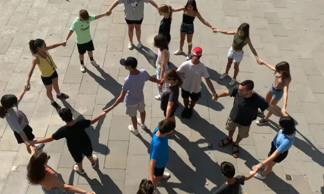 Un grupo de adolescentes participa en juegos cooperativos, tomados de la mano en un círculo en el exterior.