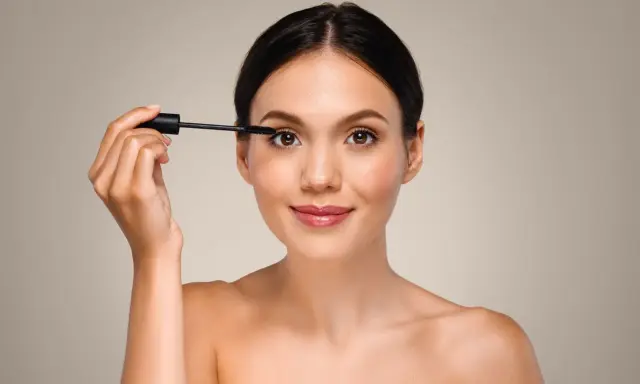 Mujer aplicando máscara de pestañas, un paso esencial para aprender como aplicar sombras de ojos principiantes y realzar la mirada.
