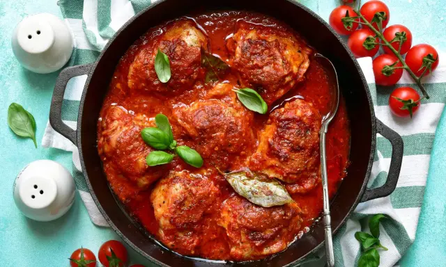 Un saporito pollo in umido, cotto lentamente in una ricca salsa di pomodoro, guarnito con basilico fresco e alloro.