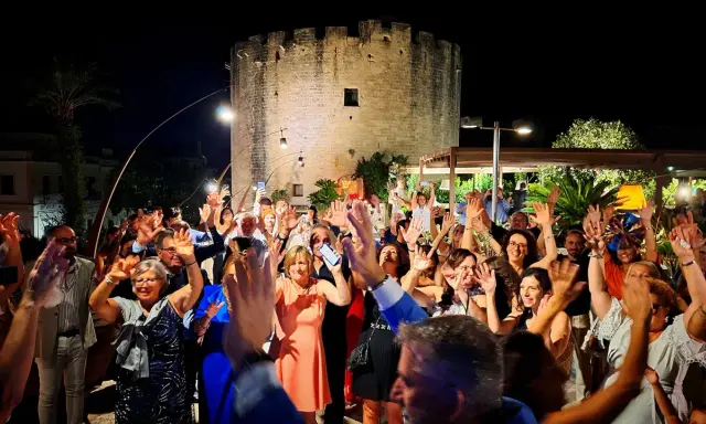 Festa con gente che alza le mani davanti a una torre antica, tipica delle sagre Salento agosto.