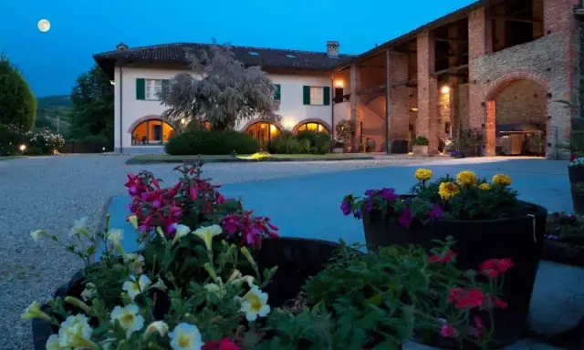Un casale illuminato al crepuscolo, con fiori colorati in primo piano. Ideale per un weekend degustazione vini Piemonte.
