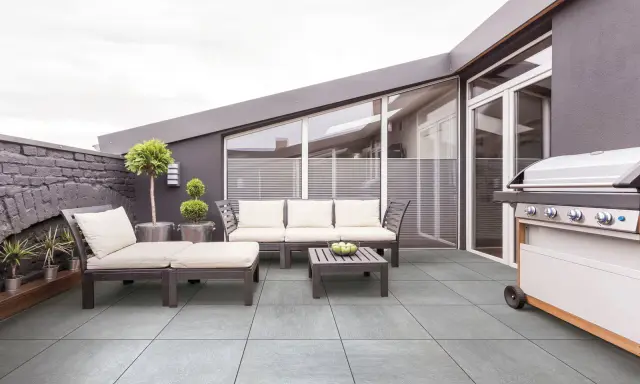 Terrasse moderne avec mobilier de jardin et barbecue. Le carrelage extérieur antidérapant est facile à nettoyer.