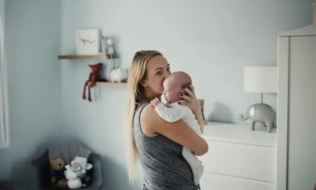 Mama tuli noworodka, który ma czkawkę. W tle pokój dziecięcy z pluszakami.