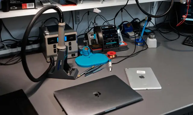 Na biurku serwisowym leży zamknięty laptop, obok tablet. W tle widać stację lutowniczą i narzędzia.