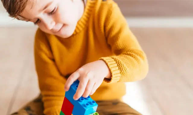 Niño concentrado jugando con bloques de construcción. Un ejemplo de cómo el juego puede ayudar a superar un retraso madurativo y TDAH.