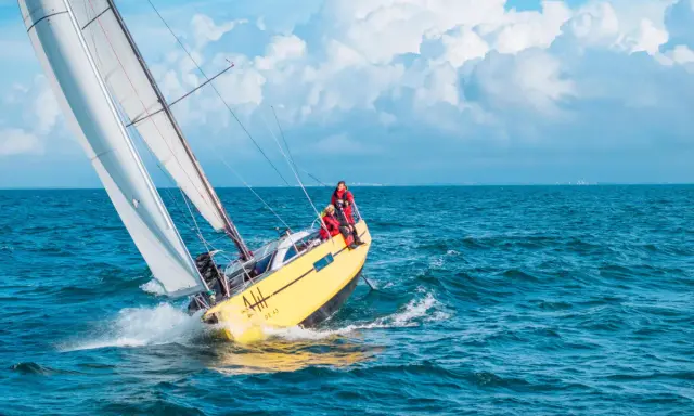 Un voilier jaune fend les vagues bleues, ses voiles blanches gonflées par le vent. L'équipage profite de cette belle journée pour faire la voile.