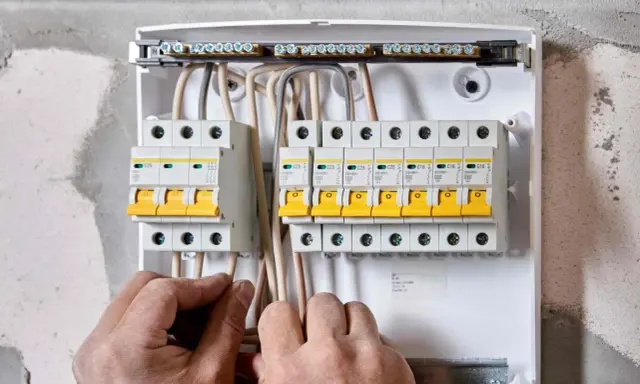 Ręce elektryka podłączają przewody do skrzynki z bezpiecznikami. To właśnie wlz co to za instalacja?