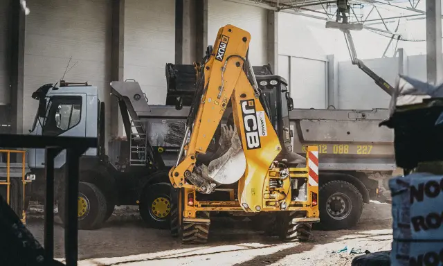 Żółty koparko-ładowarka JCB i ciężarówka na placu budowy.