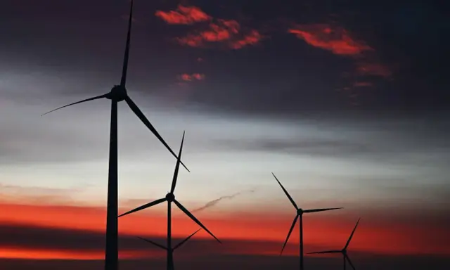 Silhouetten von Windkraftanlagen in den Niederlanden vor einem dramatischen Sonnenuntergang mit roten Wolken.