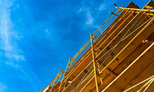 Estructura amarilla de madera y metal, que es una cimbra, contra un cielo azul con nubes finas.