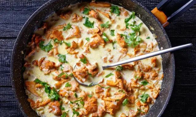 Pfifferlinge in cremiger Rahmsauce, garniert mit frischer Petersilie, in einer Pfanne. Ein Löffel ragt aus der köstlichen Speise.