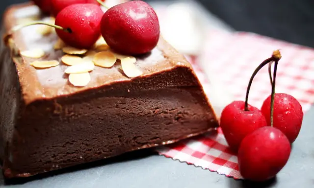 Une délicieuse marquise au chocolat, garnie de cerises fraîches et d'amandes effilées, prête à être dégustée.