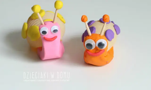 Dwa urocze ślimaki z plasteliny, jeden różowy, drugi pomarańczowy, z wielkimi oczami i uśmiechem.