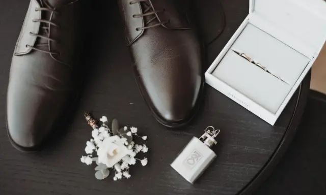 Eleganckie brązowe buty męskie, butonierka, pierścionki w pudełku i piersiówka.